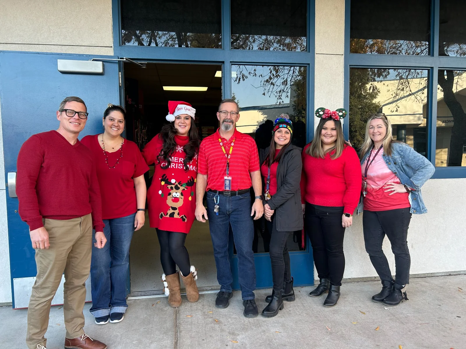 A group of educators in festive red clothing outside a school building.