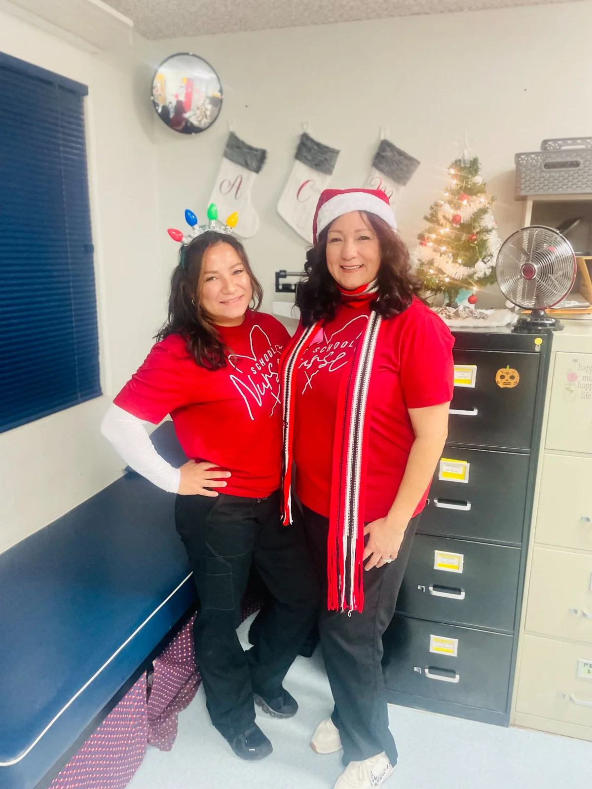 Two educators wearing festive red clothing inside a school office.
